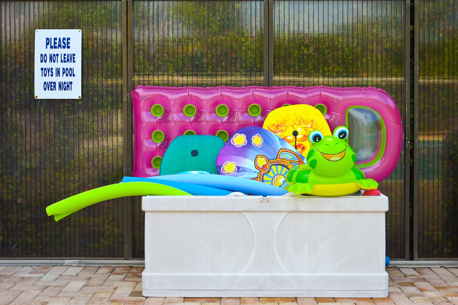 A storage bin by a pool contains various colorful pool toys.