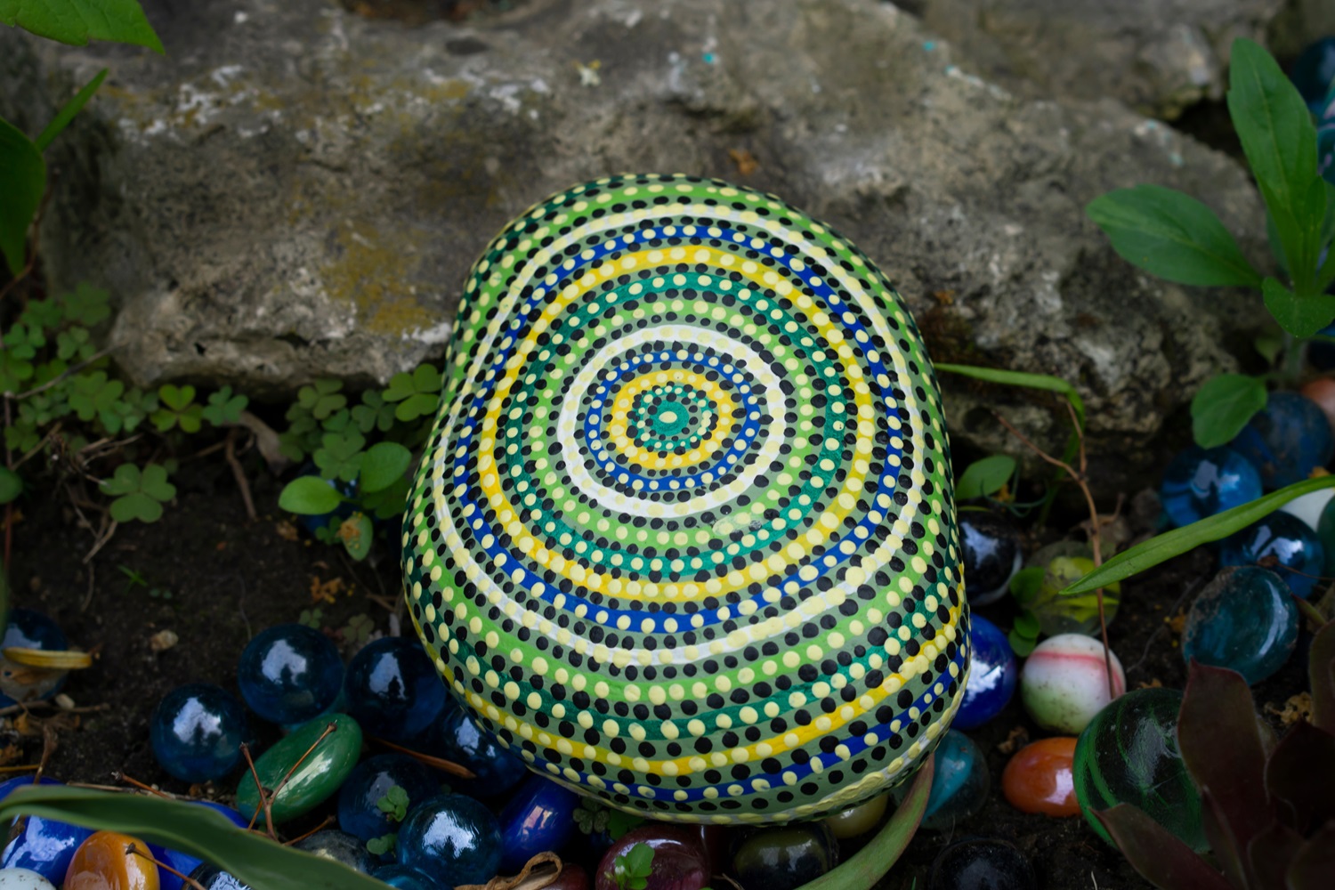 A mandala painted rock with colorful, concentric circles among glass marbles