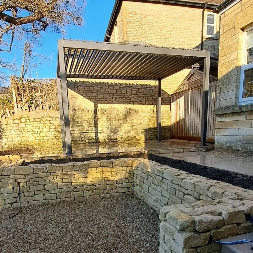 Stone patio with a modern pergola in a backyard surrounded by stone walls