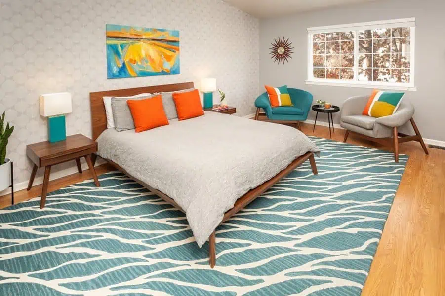 Modern bedroom with mid-century furniture, colorful accents, and teal patterned rug.