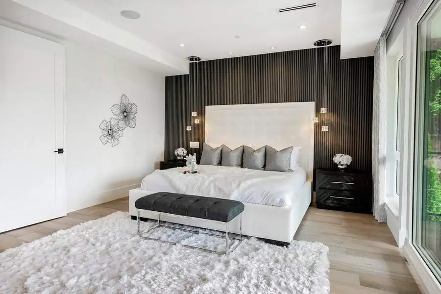 Modern bedroom with a white tufted bed, dark accent wall, hanging pendant lights, and a fluffy white rug.