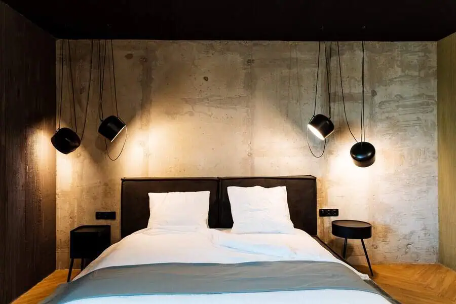 Industrial bedroom with concrete walls, minimalist decor, and black hanging pendant lights.