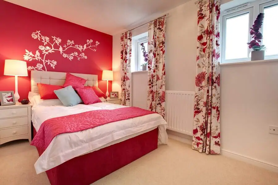 Bright bedroom with red accent wall, floral curtains, and matching red bedding.