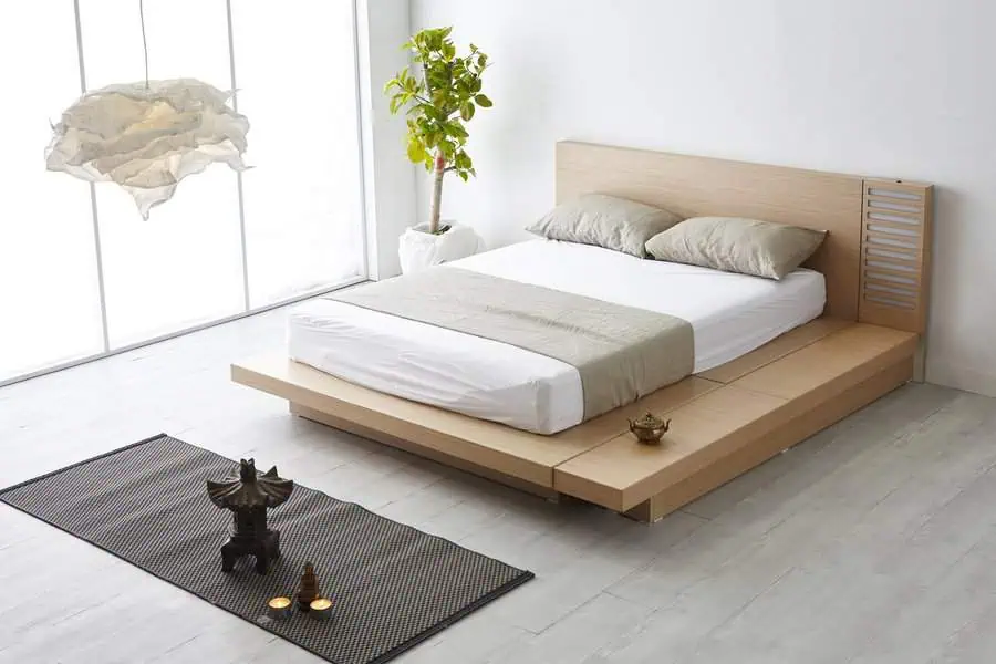 Minimalist bedroom with low platform bed, neutral bedding, indoor plant, and modern decor.