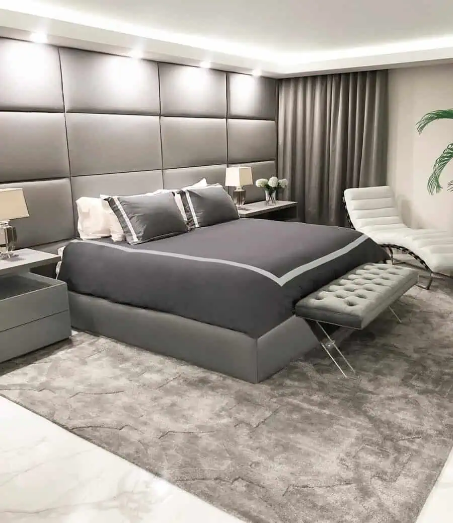 Sleek modern bedroom with grey upholstered walls, matching bedding, and a chaise lounge.