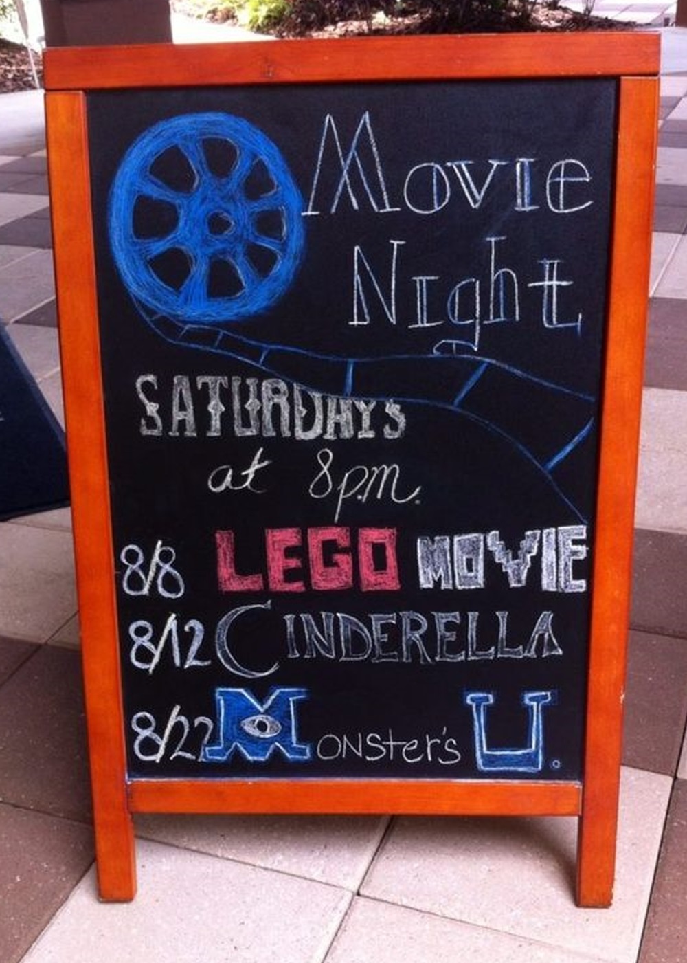 Chalkboard sign advertising movie nights featuring "LEGO Movie", "Cinderella", and "Monster's U".