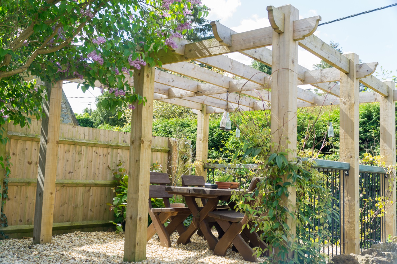 Wooden pergola over a garden dining area with wooden furniture and greenery