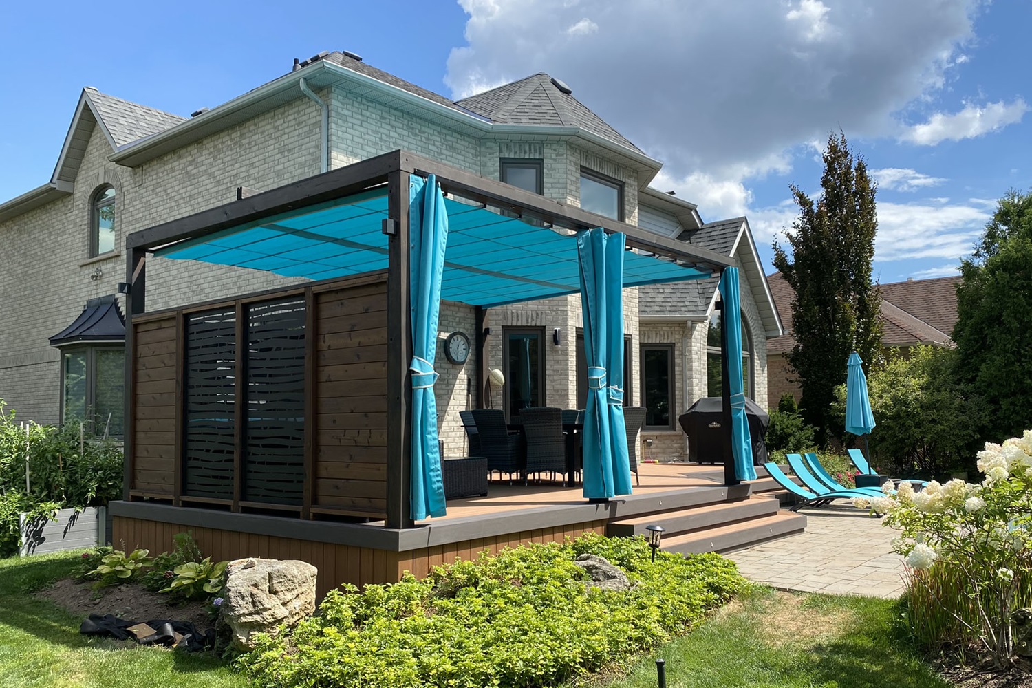 House with backyard deck, pergola with blue curtains, and turquoise lounge chairs