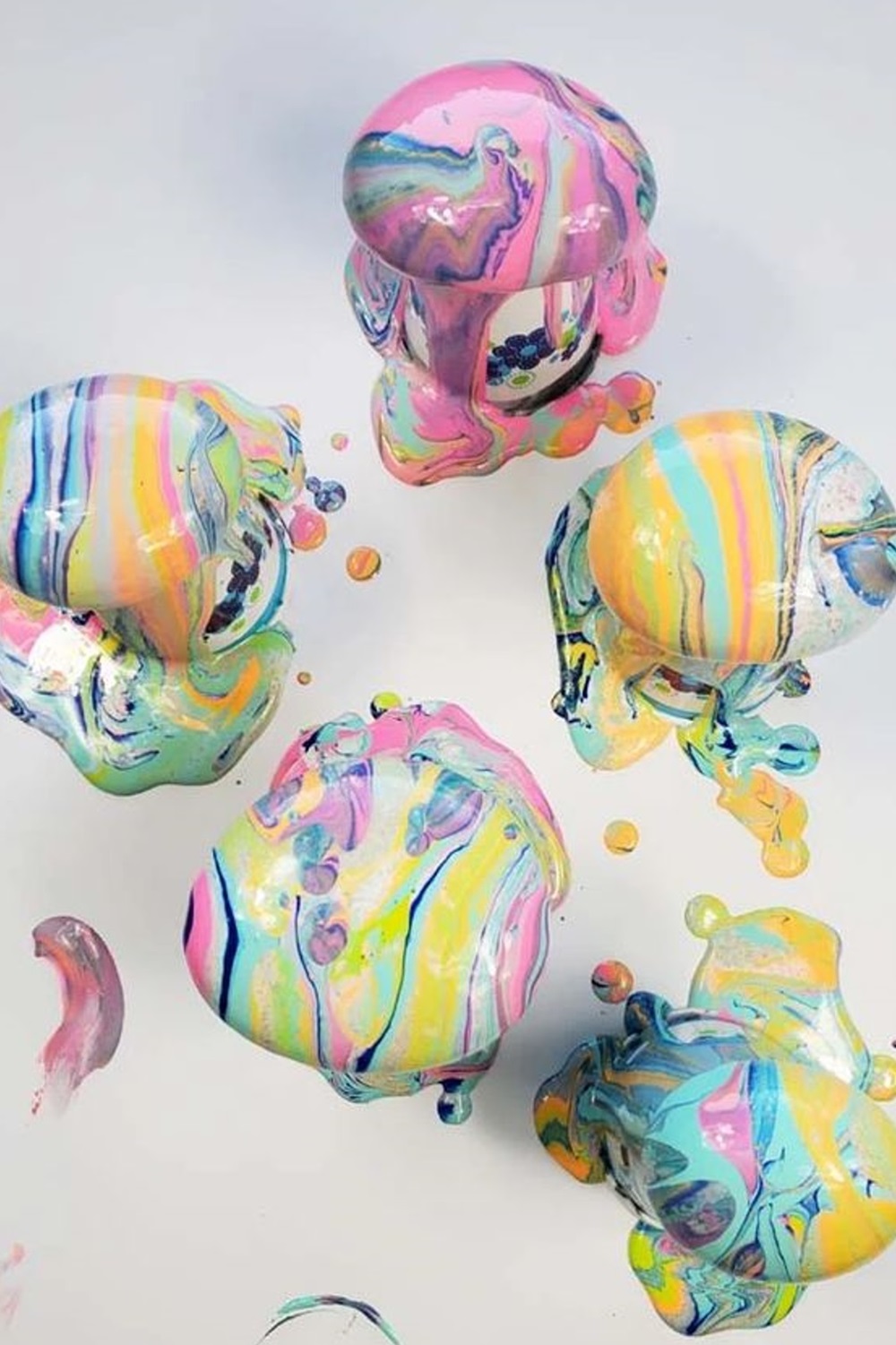 Colorful, marbled paint oozing over four round stones on a white surface