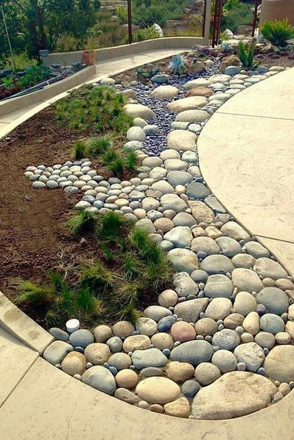 A curved garden featuring assorted rocks and grass patches beside a concrete path