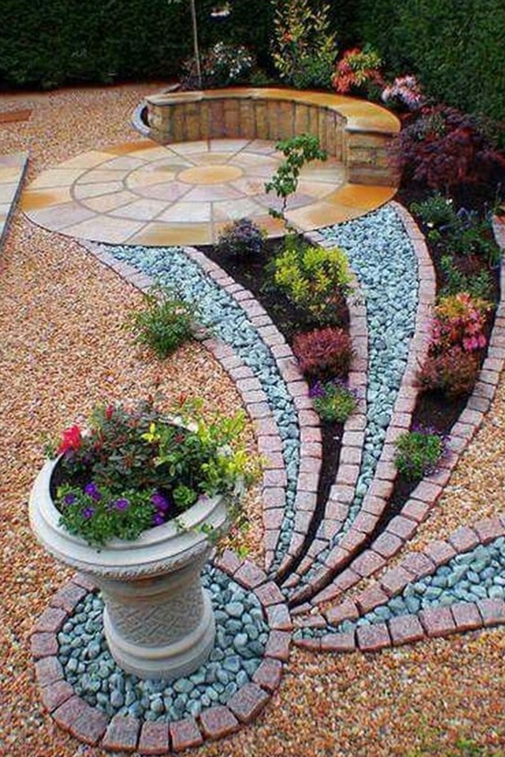 A modern garden with patterned gravel, stone pathways, plants, and a circular patio