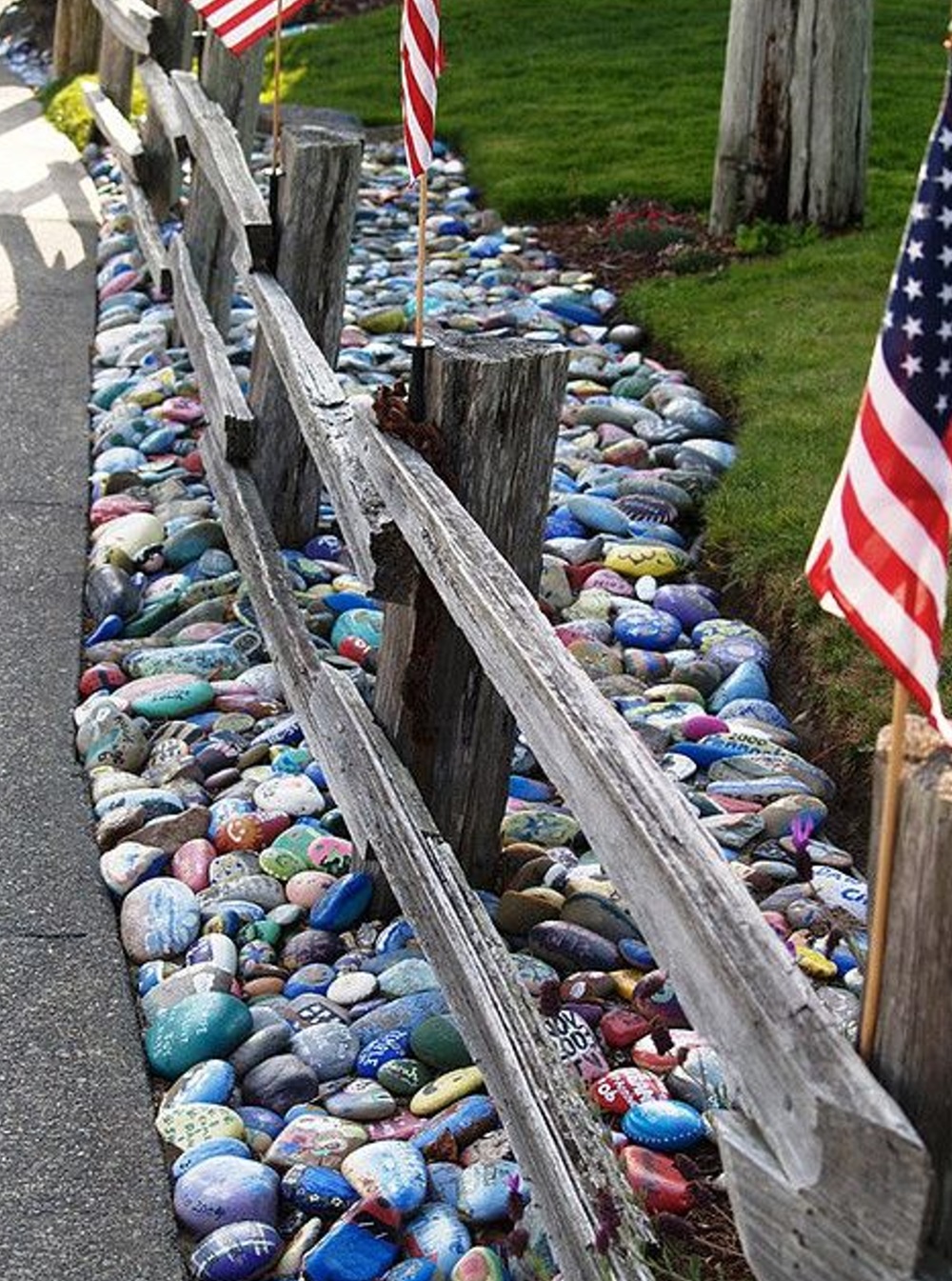 Painted rocks along wooden fence with American flags on lawn