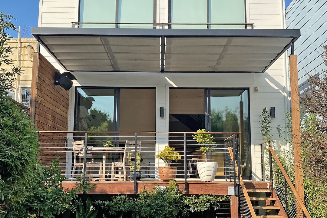 Modern two-story house with shaded patio, potted plants, and glass doors