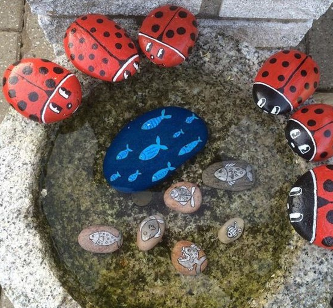 Painted ladybug and fish rocks surrounding a small stone basin