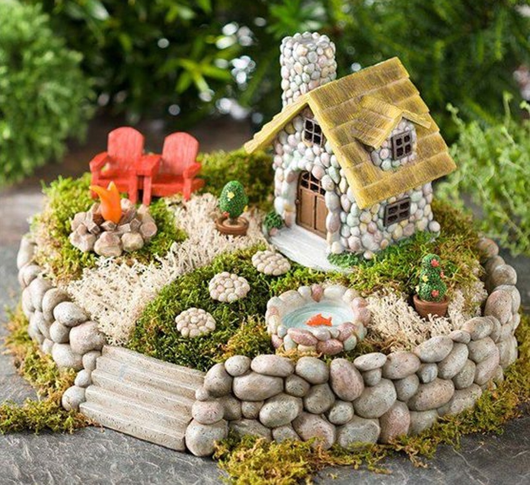 Miniature stone cottage with yard, pond, red chairs, and campfire on a mossy base