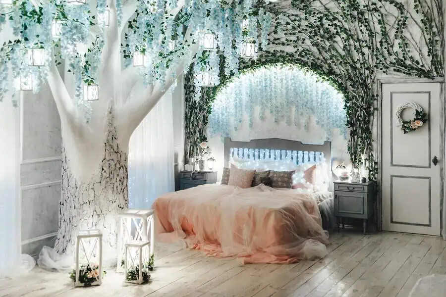 Whimsical bedroom with a fairy tale theme, featuring a large decorative tree, floral canopy, and soft pastel bedding.