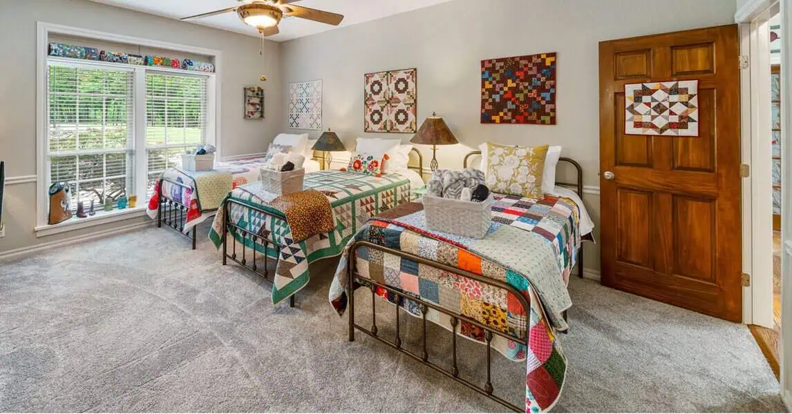 Cozy bedroom with twin beds, colorful patchwork quilts, and craft-themed decor.