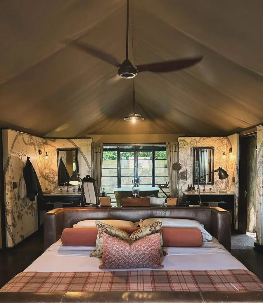 Rustic bedroom with a ceiling fan, leather headboard, decorative pillows, and a map-themed wallpaper.