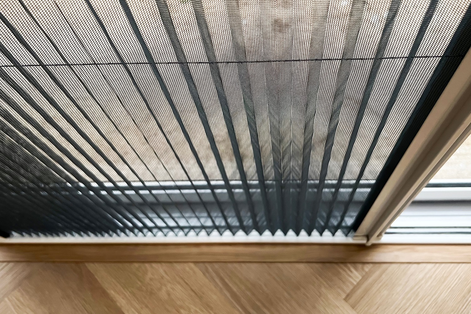 Close-up of a pleated mesh screen door partially open. The screen forms a zigzag pattern.