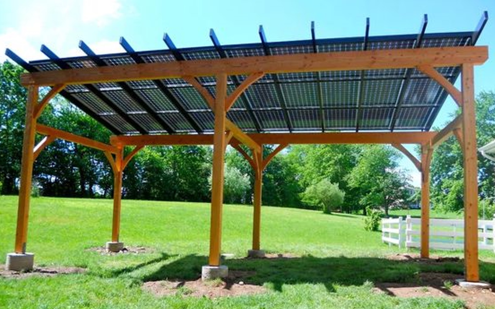 Wooden pergola with solar panels in a grassy backyard, surrounded by trees and fence