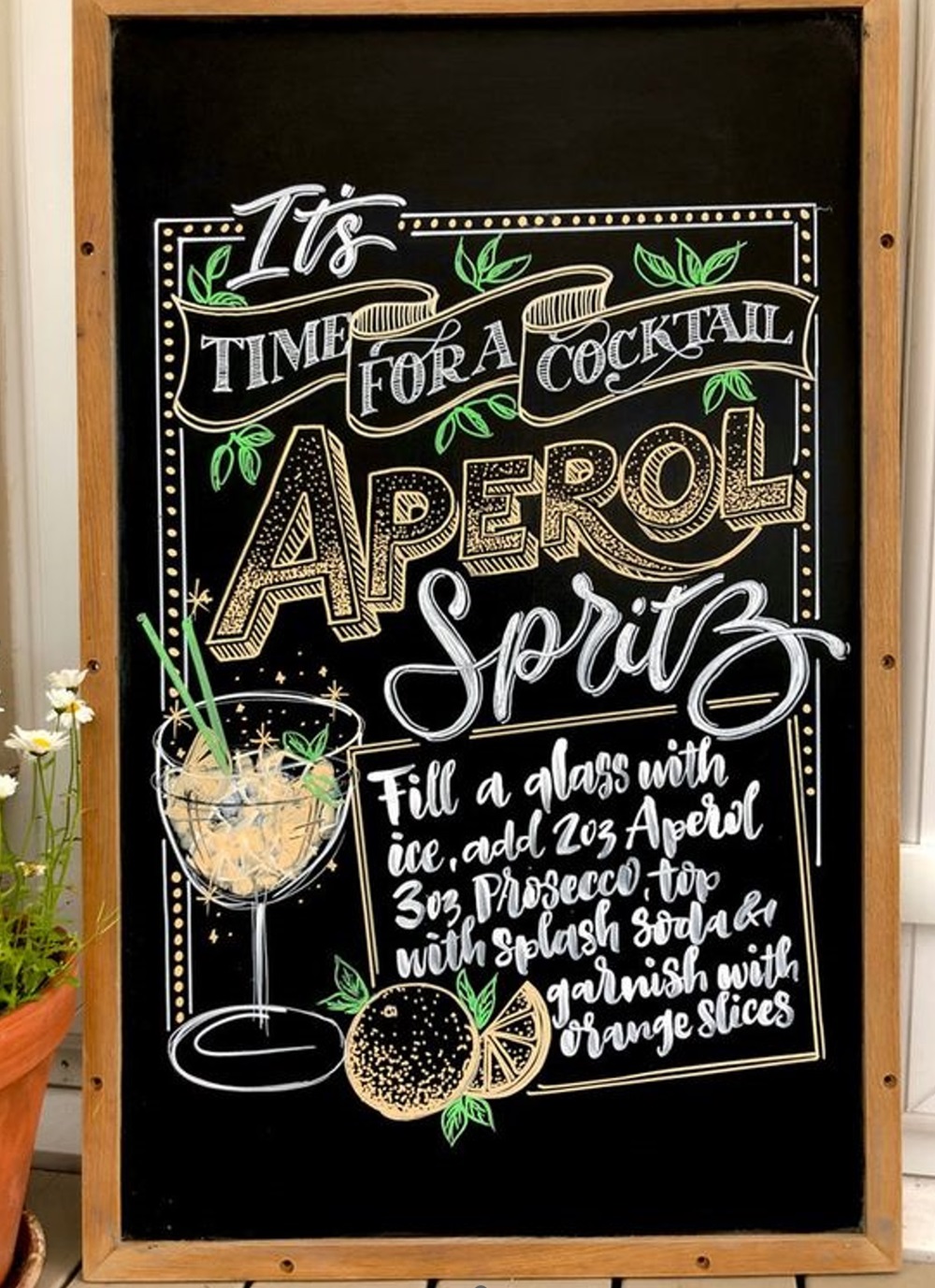 Chalkboard sign with Aperol Spritz cocktail recipe and decorative drawings.