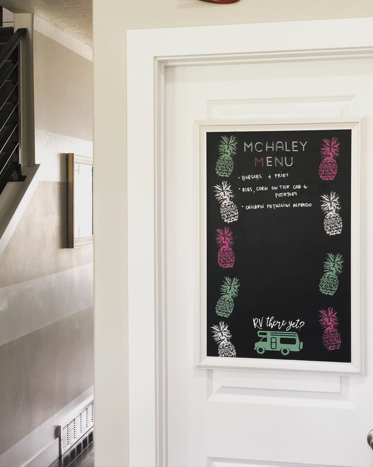 Chalkboard menu on a white door with colorful pineapples and a green RV truck drawing.