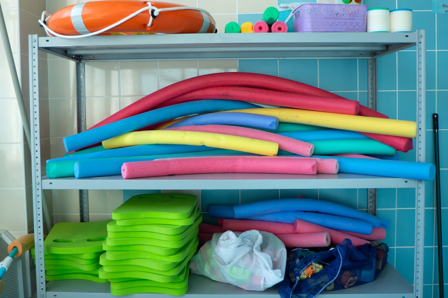 Colorful pool noodles, kickboards, and flotation devices stacked on metal shelves.