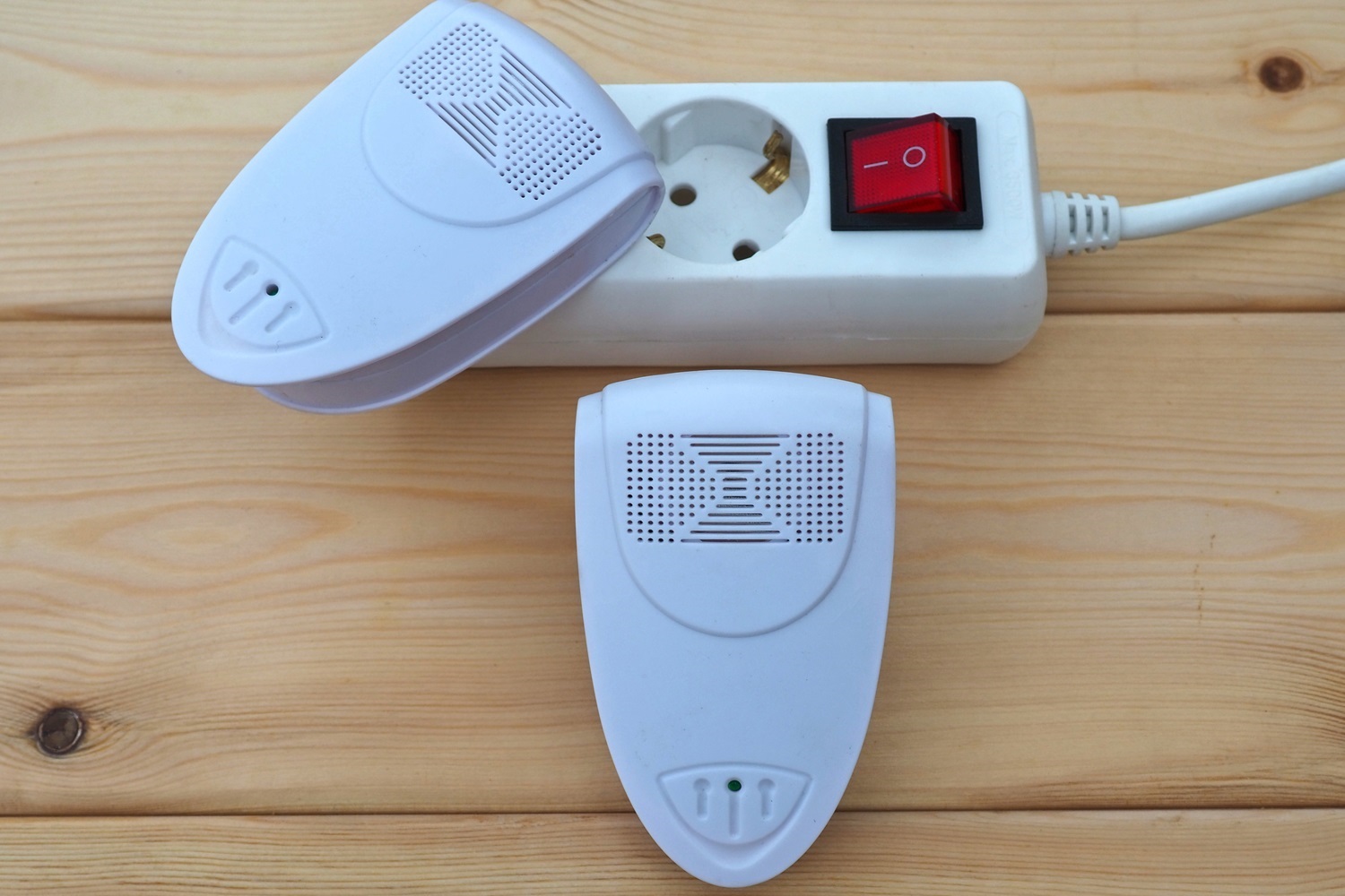 Two white ultrasonic pest repellers near a power strip.