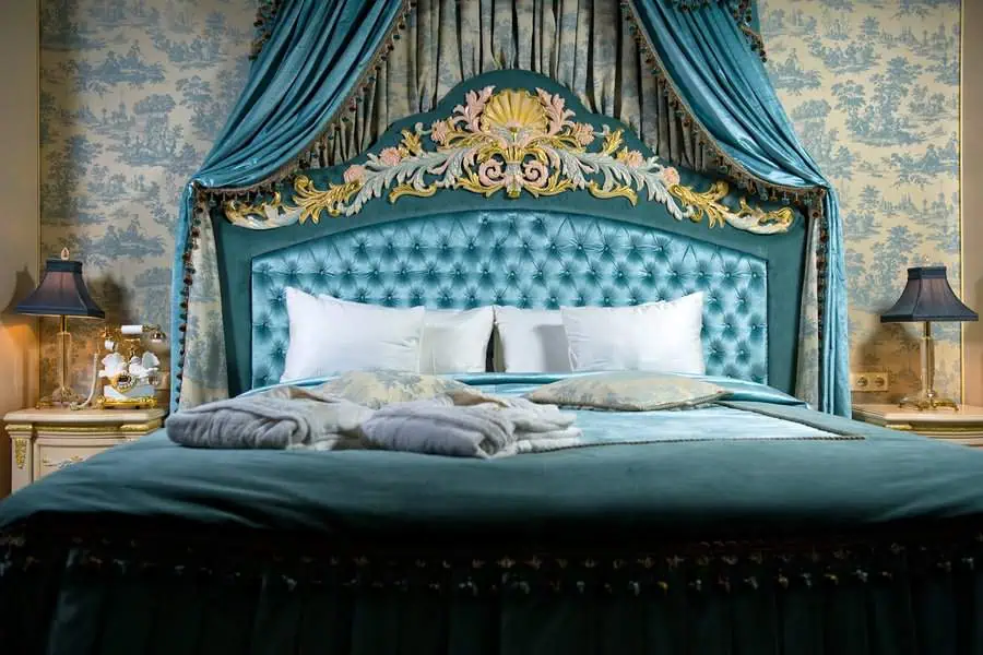 Opulent bedroom with an ornate turquoise canopy bed, luxurious bedding, and elegant decor.