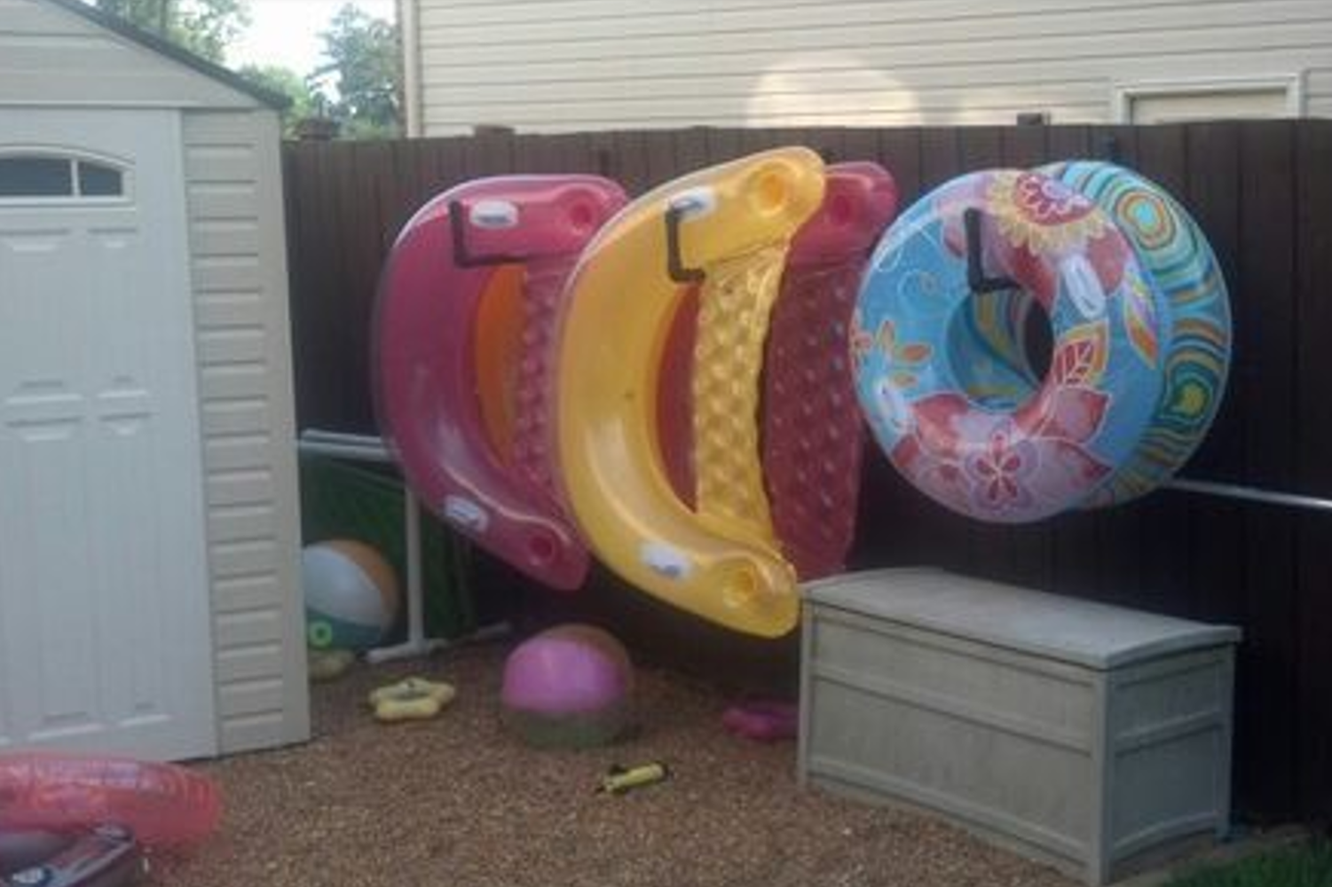 Colorful pool floats hang neatly on a brown fence on a wall-mounted hooks.