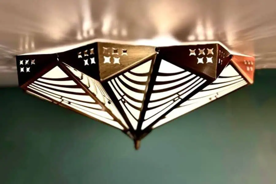 An intricate, geometric ceiling light fixture with a brass finish, casting warm, patterned light.