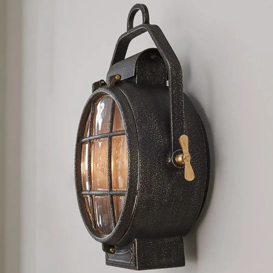 An antique-style, wall-mounted lantern with a metal frame and glass cover featuring a crossbar design