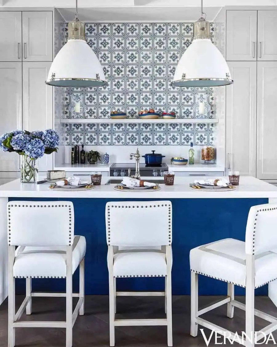 Modern kitchen with blue and white tile, island, white barstools, and pendant lights