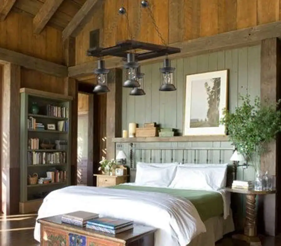 Cozy bedroom with wooden beams, a bookshelf, greenery, and a green bedspread under a hanging light.