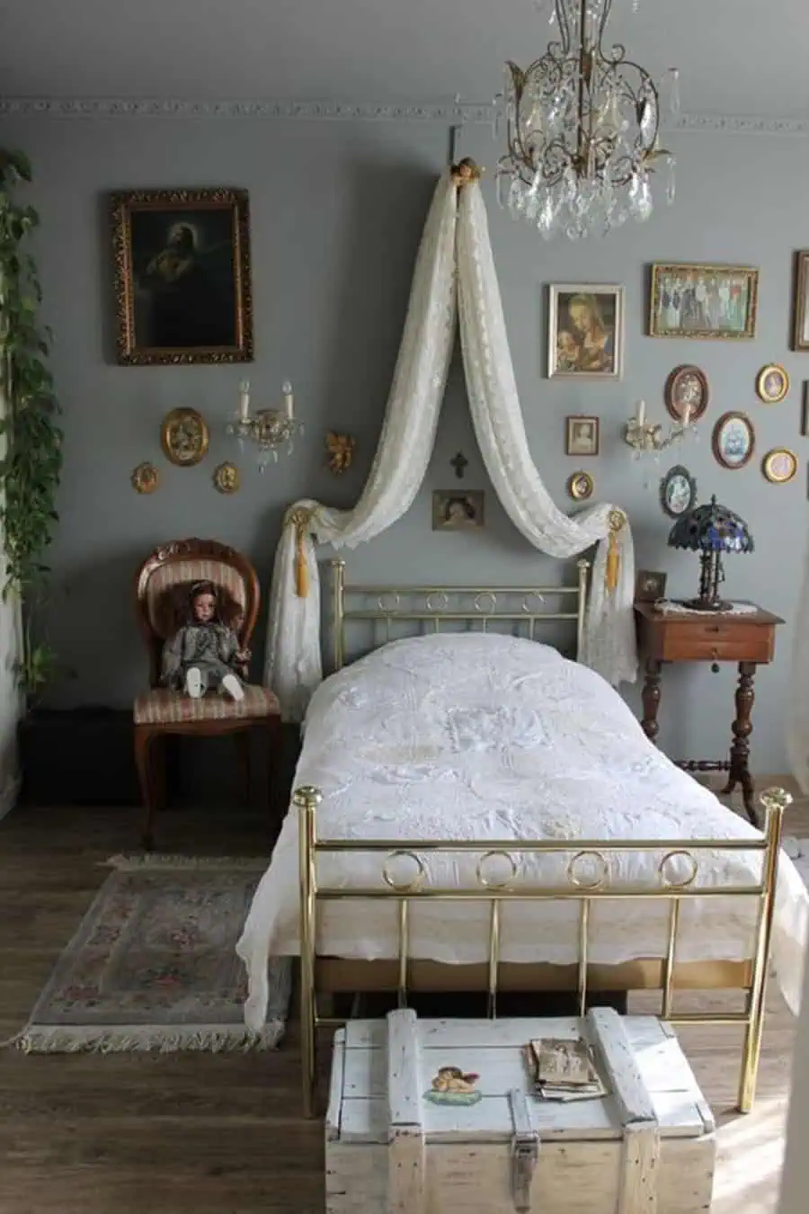 A vintage-style bedroom with an ornate bed, chandelier, framed pictures on the walls, and a draped canopy over the bed