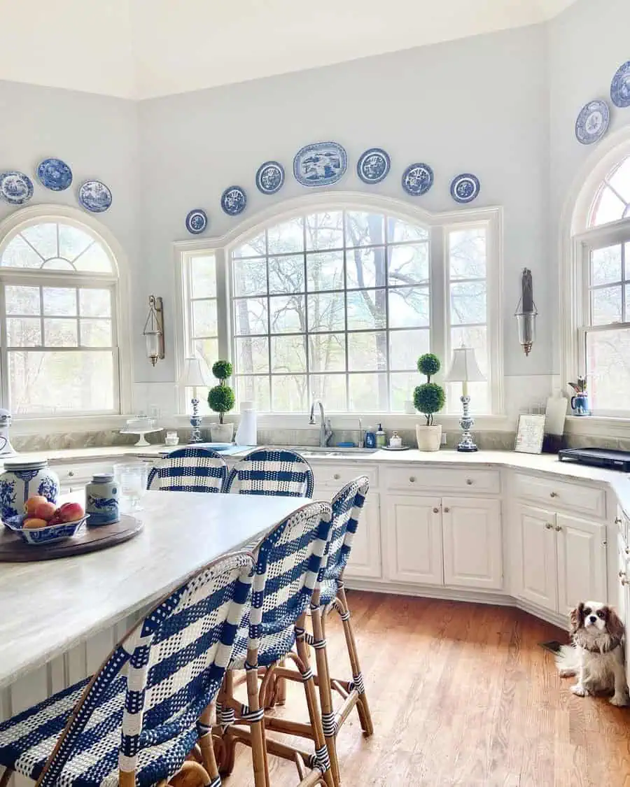 A bright kitchen with white cabinetry, blue checkered chairs, and decorative plates on the wall above the windows.