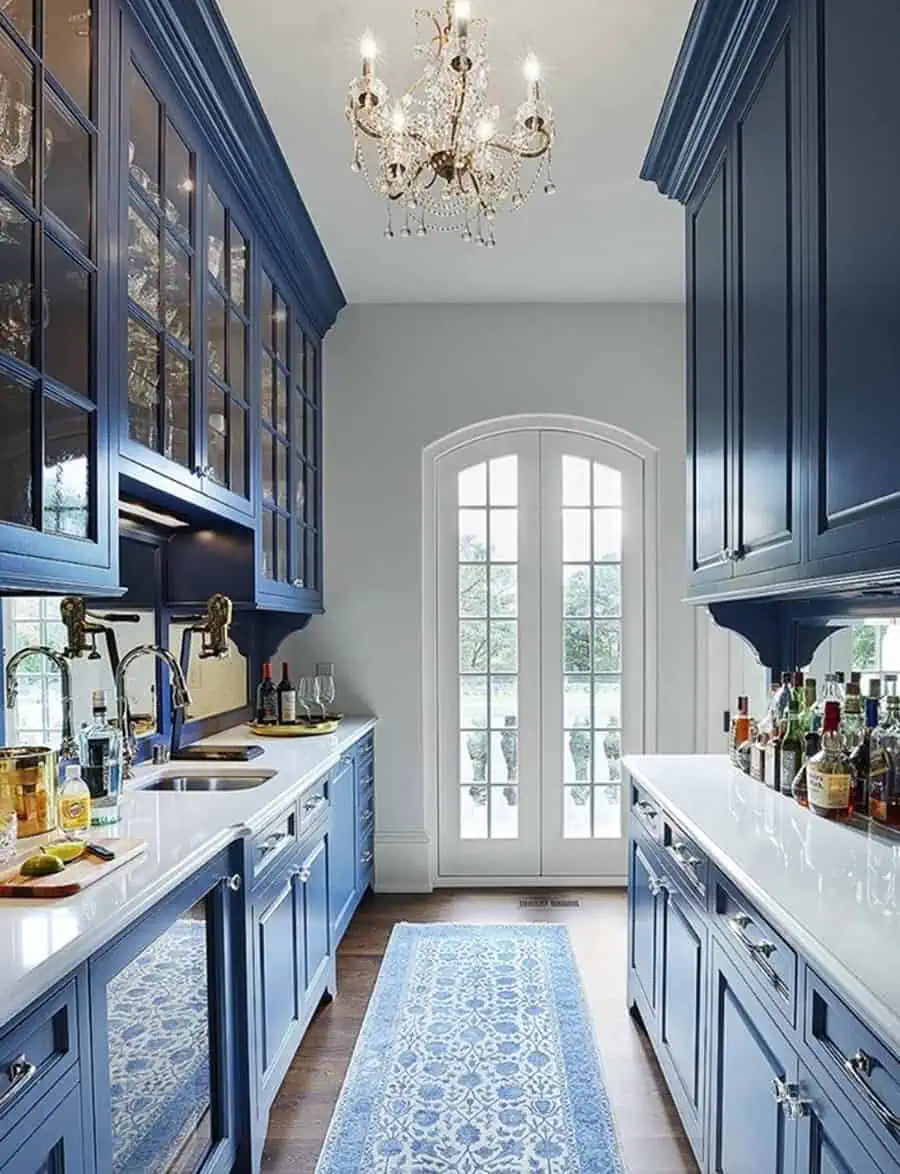 A narrow kitchen with blue cabinetry, a chandelier, and a patterned runner rug.