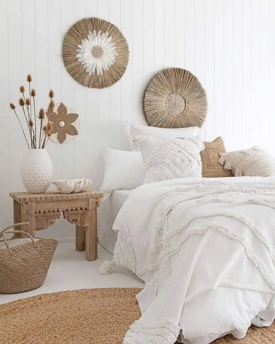 Bedroom with white bedding, wicker wall decor, wooden furniture, and dried plants in a vase.