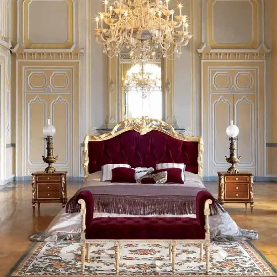 A luxurious bedroom features a red velvet upholstered bed with ornate gold accents, flanked by two wooden nightstands.