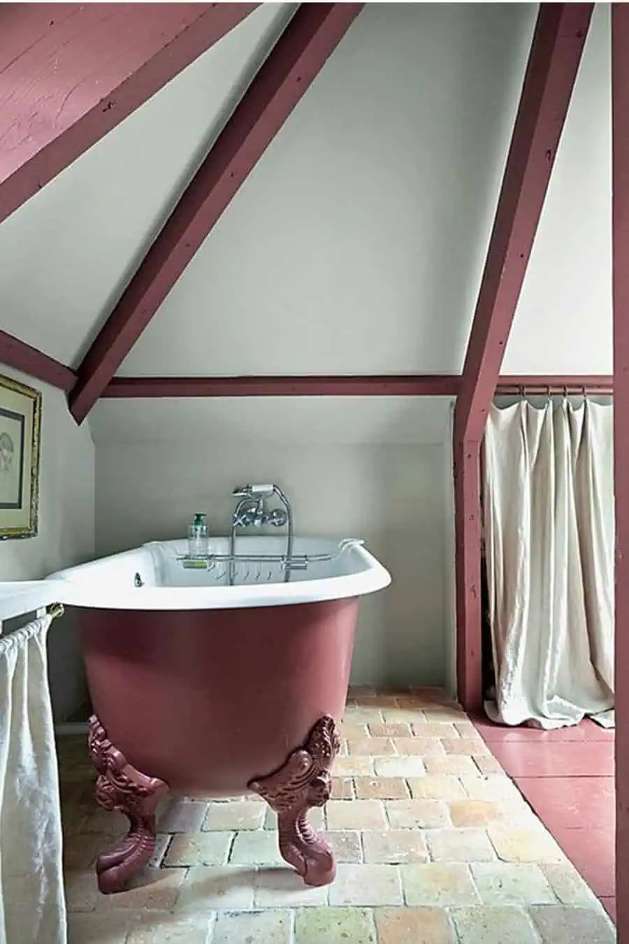 Vintage bathroom with a burgundy clawfoot tub, exposed beams, and rustic brick flooring.