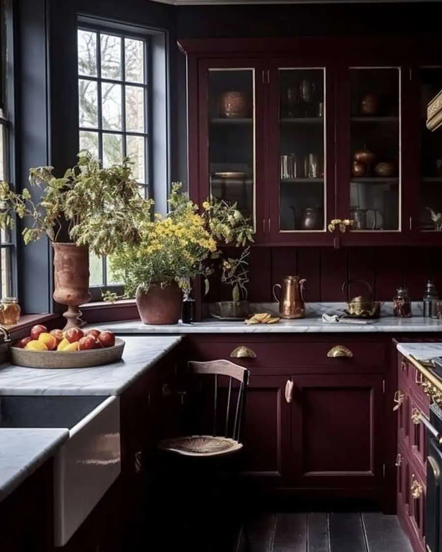 Cozy kitchen with burgundy cabinets, marble countertops, and rustic decor, featuring fresh flowers and fruit.