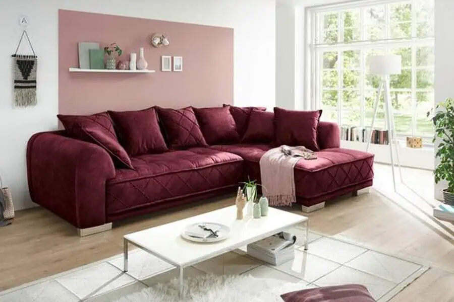 Bright living room with a burgundy sectional sofa, light pink accent wall, and large windows.