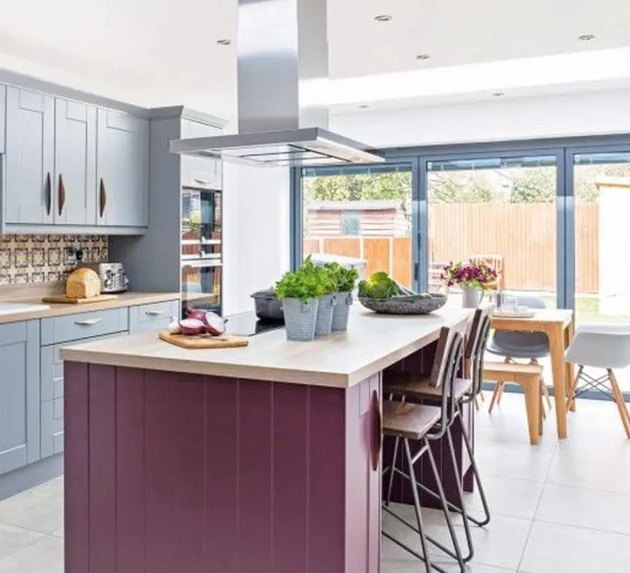 Modern kitchen with light gray cabinets, a burgundy island, and a bright dining area with garden views.