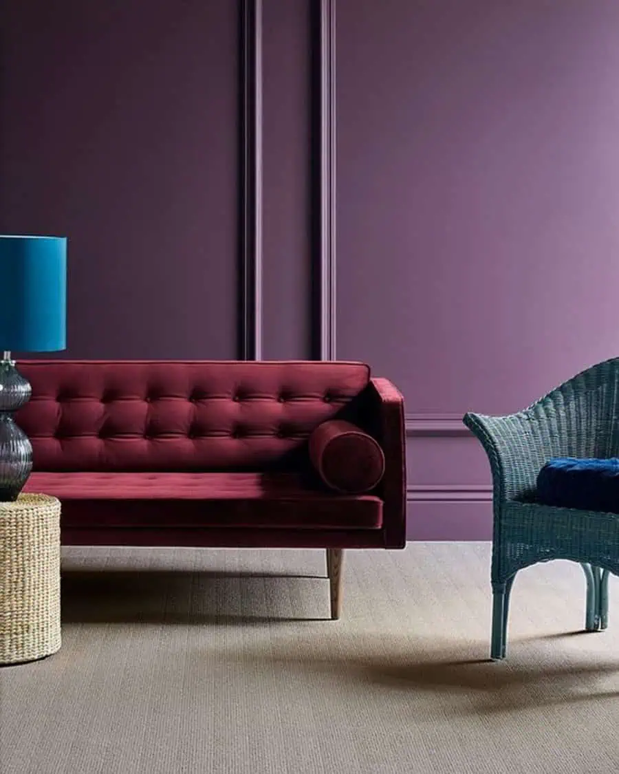 Stylish room with a burgundy tufted sofa, purple walls, and a teal wicker chair.