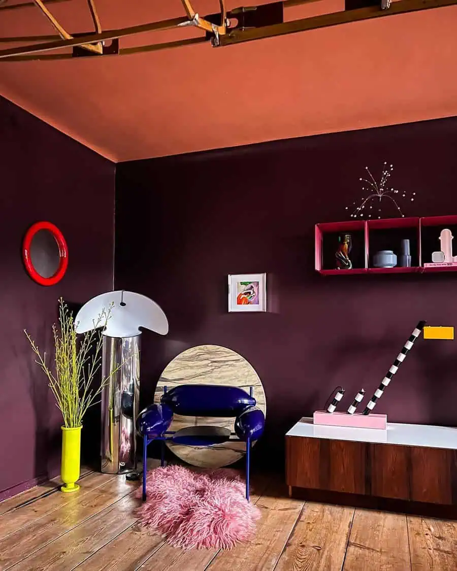 A bold room with dark purple walls, a peach ceiling, modern furniture, a yellow vase with green plants, and blue chair.