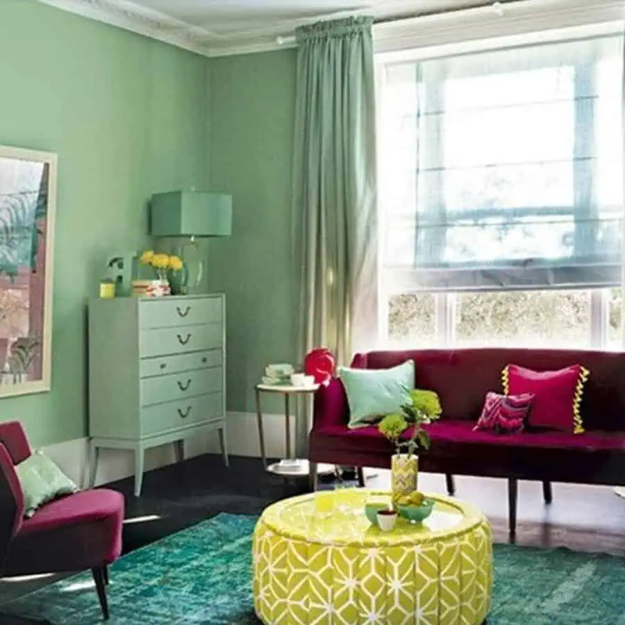 Vibrant living room with mint green walls, burgundy sofa, and a yellow patterned ottoman as the centerpiece.