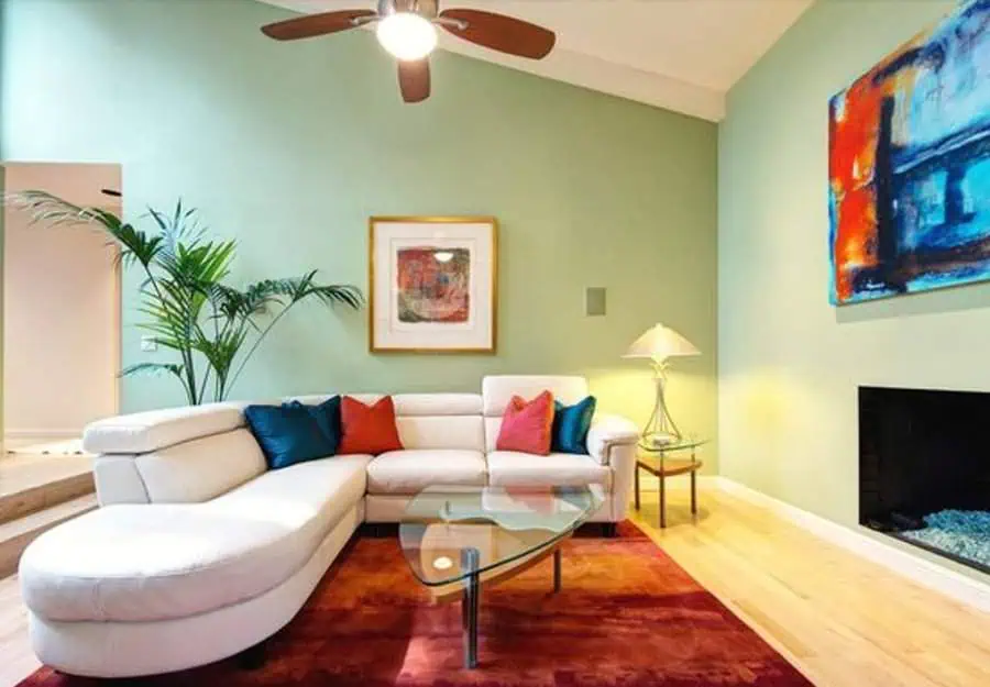 Contemporary living room with a white sectional sofa, colorful pillows, mint green walls, and abstract artwork.