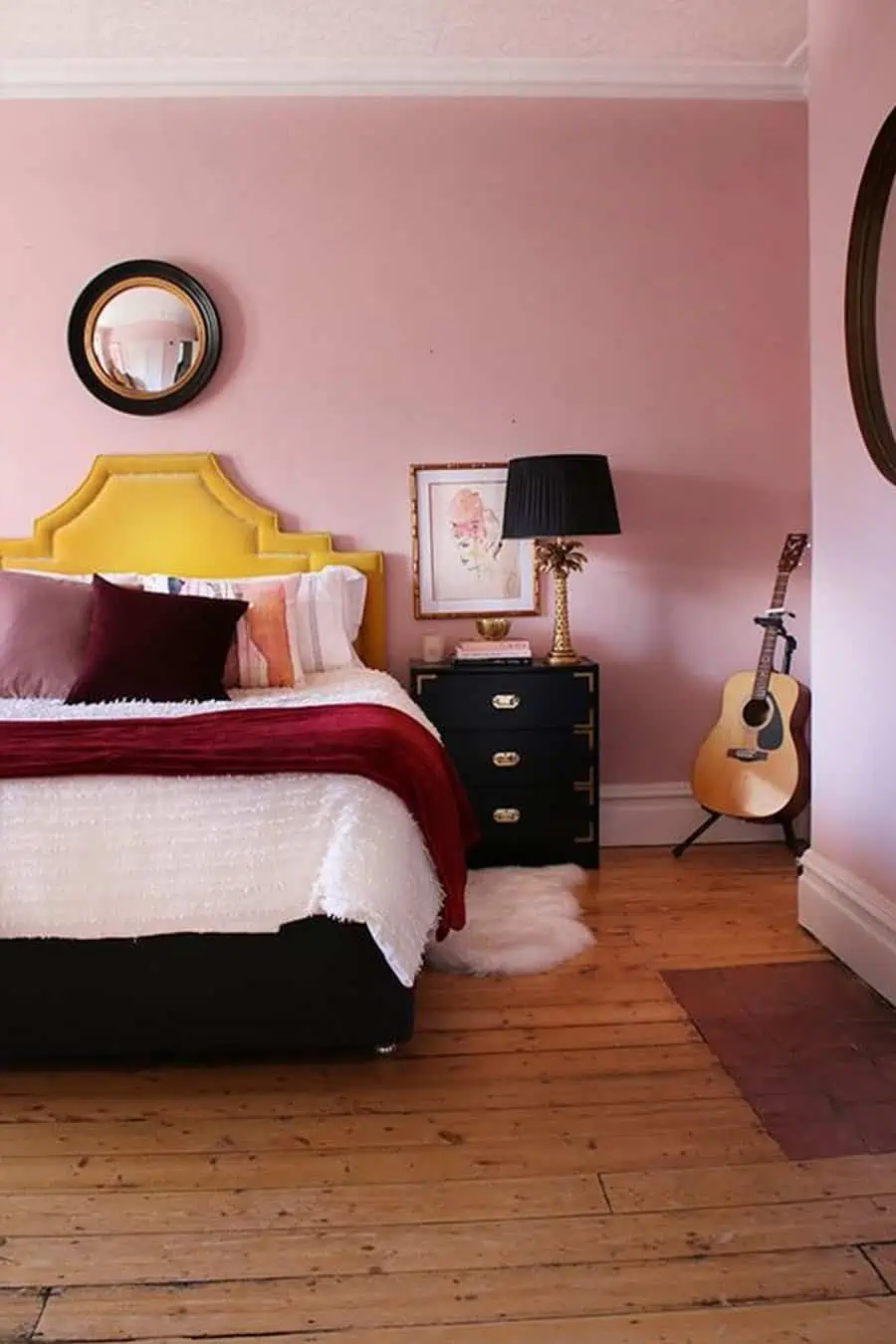 Bedroom with pink walls, yellow headboard, and neatly made bed with red, white, and brown bedding. 