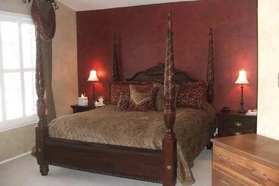 Traditional bedroom with a four-poster bed, burgundy accent wall, and warm lighting from bedside lamps.