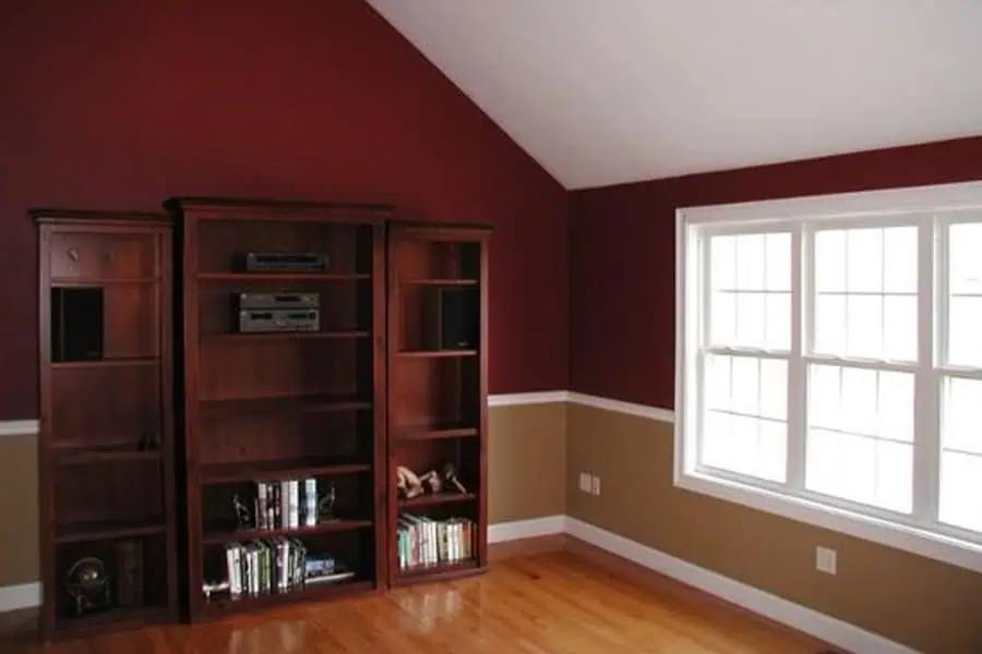 Simple room with burgundy and tan walls, wooden bookshelves, and natural light from a large window.